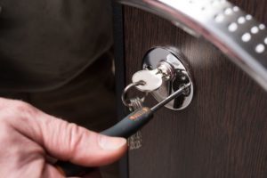 Someone is using a spanner instrument to screw up the lock on a wooden door, demonstrating a repair or installation process